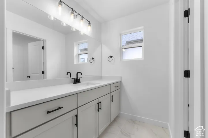 Bathroom featuring a light-toned vanity, white countertop with an integrated sink, matte black hardware, large wall-mounted mirror, and tile flooring