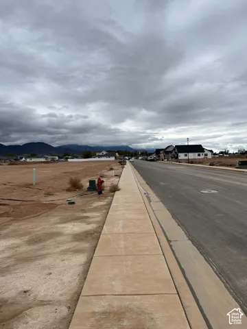 Cleared residential lot featuring paved street access, concrete sidewalk, utility infrastructure, and mountain surroundings