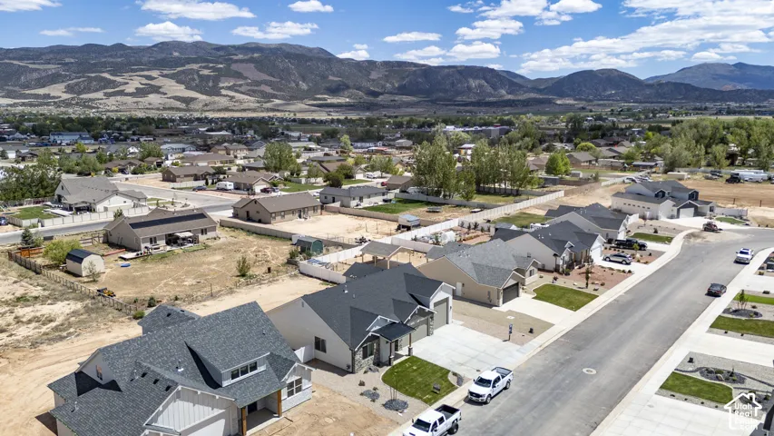 Aerial perspective of a suburban neighborhood featuring asphalt roadways, single-story residences with shingled roofs, manicured lawn patches, and a prominent mountain range backdrop