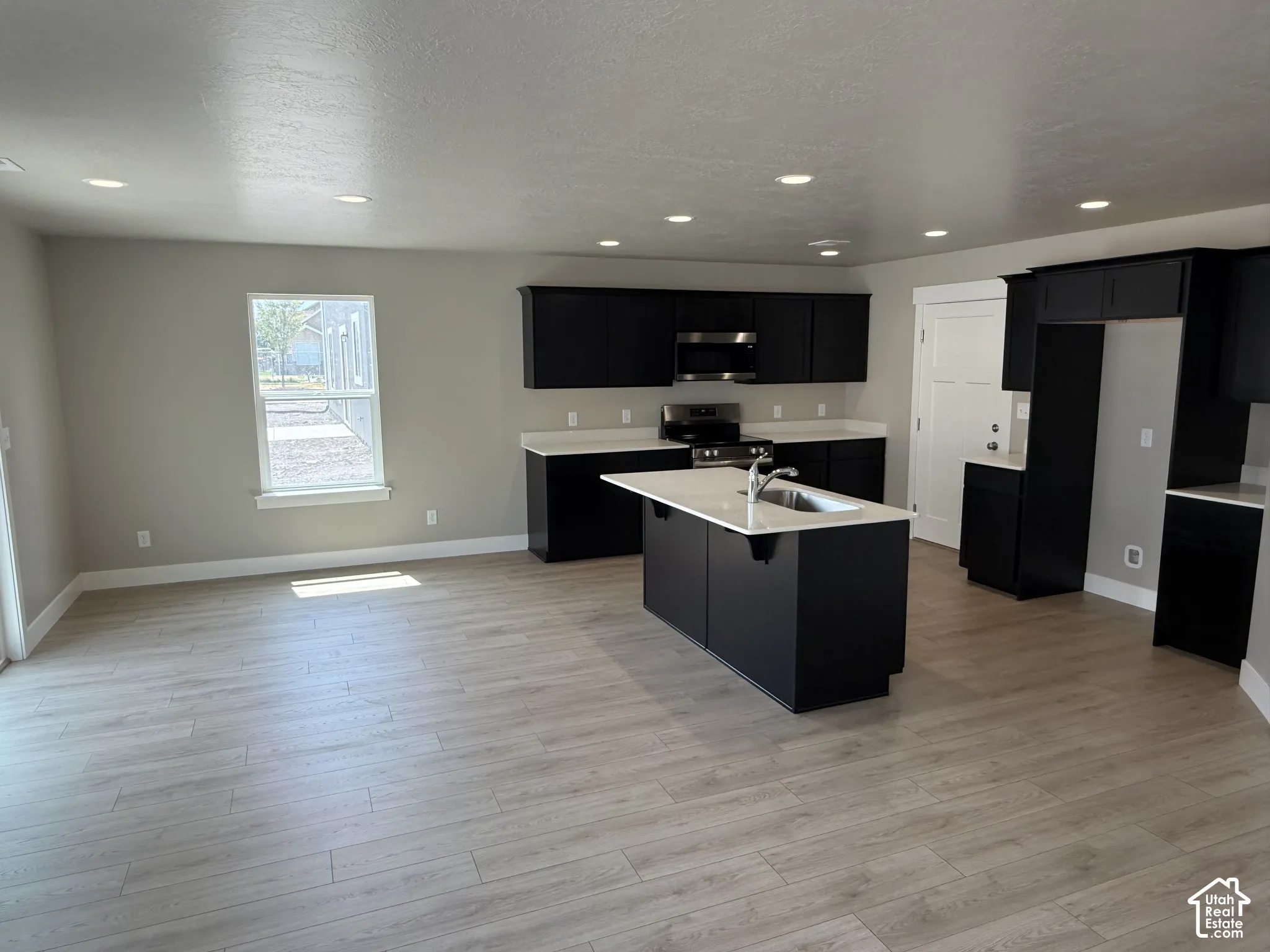 Kitchen featuring dark cabinetry, an island with a light-toned countertop, integrated stainless steel appliances, recessed lighting, and wood-finish flooring