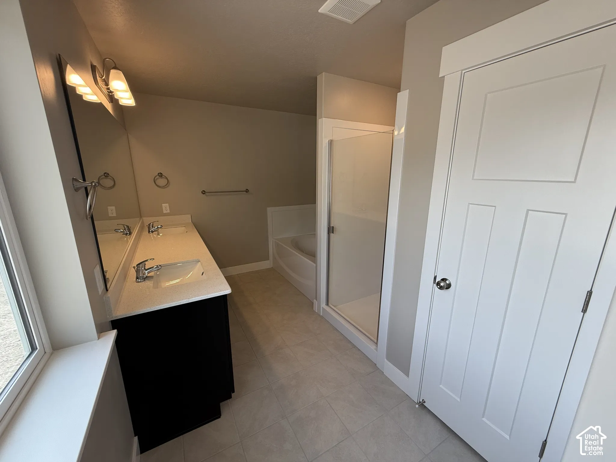 Dual-sink vanity with a quartz countertop, glass-enclosed shower, soaking tub, and large wall-mounted mirror