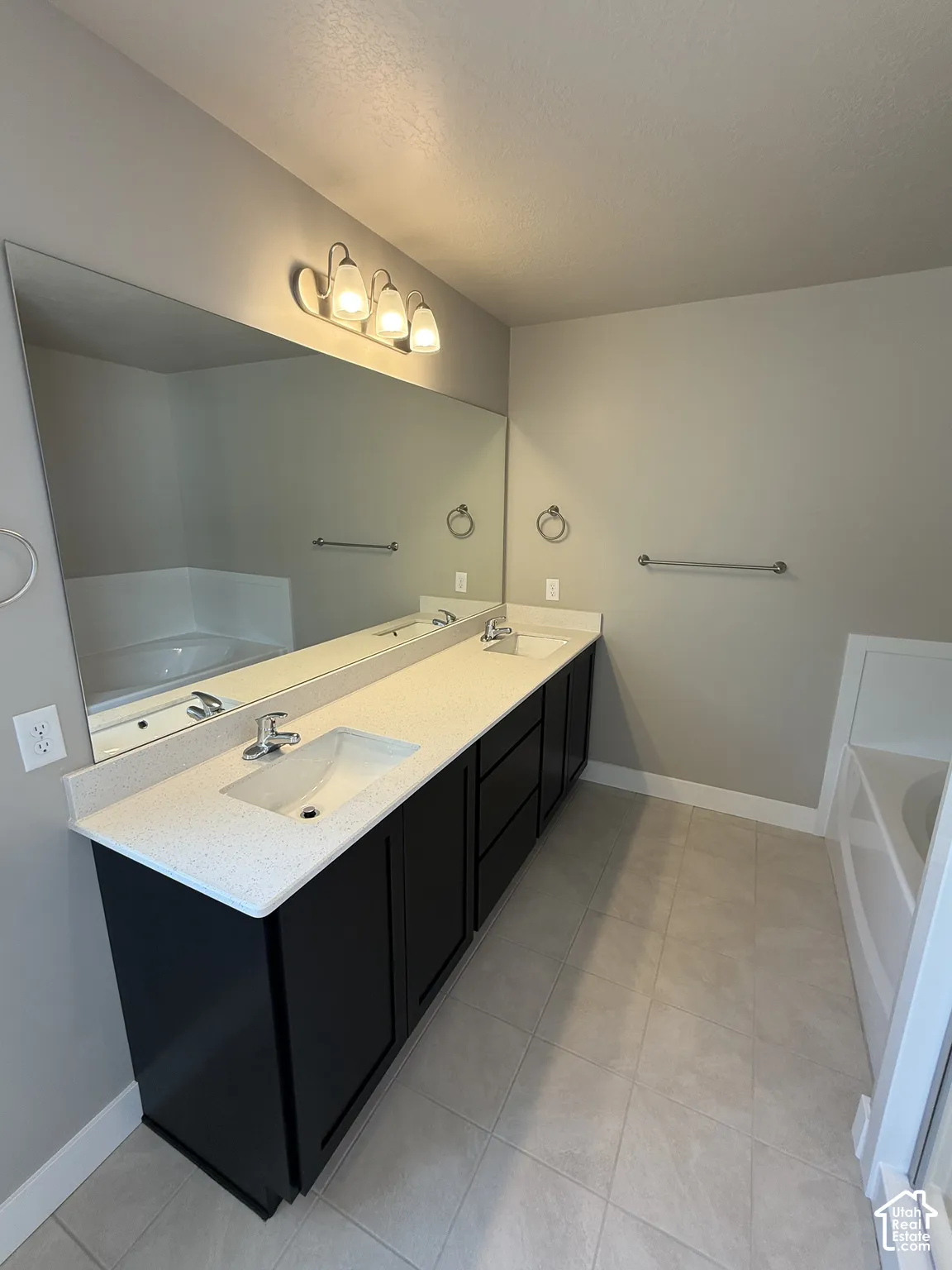 Double vanity featuring dark cabinetry, solid-surface countertop with dual rectangular sinks, a full-width mirror, and three-bulb vanity lighting
