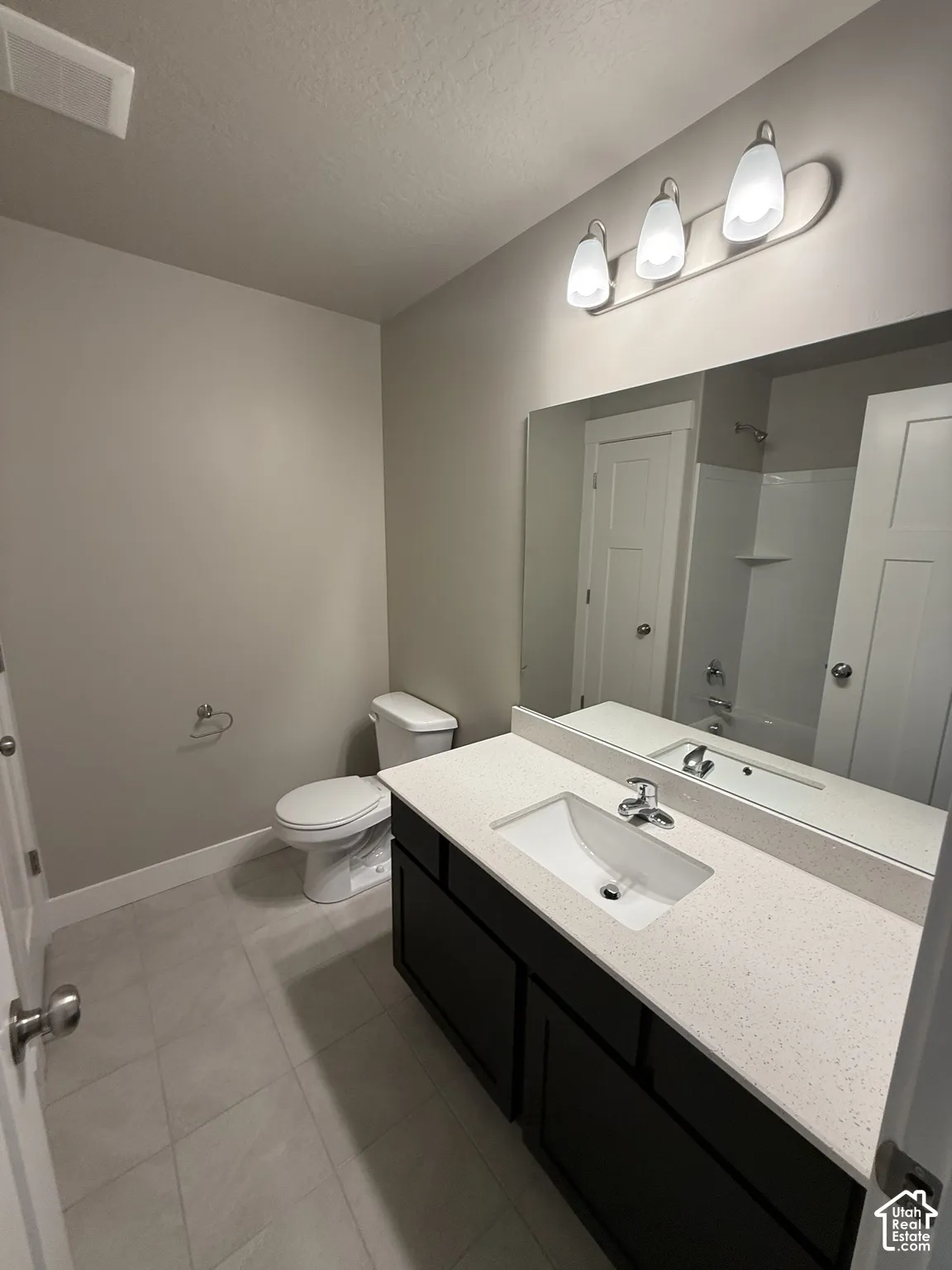 Bathroom featuring a dark-finish vanity with a light stone-composite countertop, integrated rectangular sink, large wall-mounted mirror, and tile flooring
