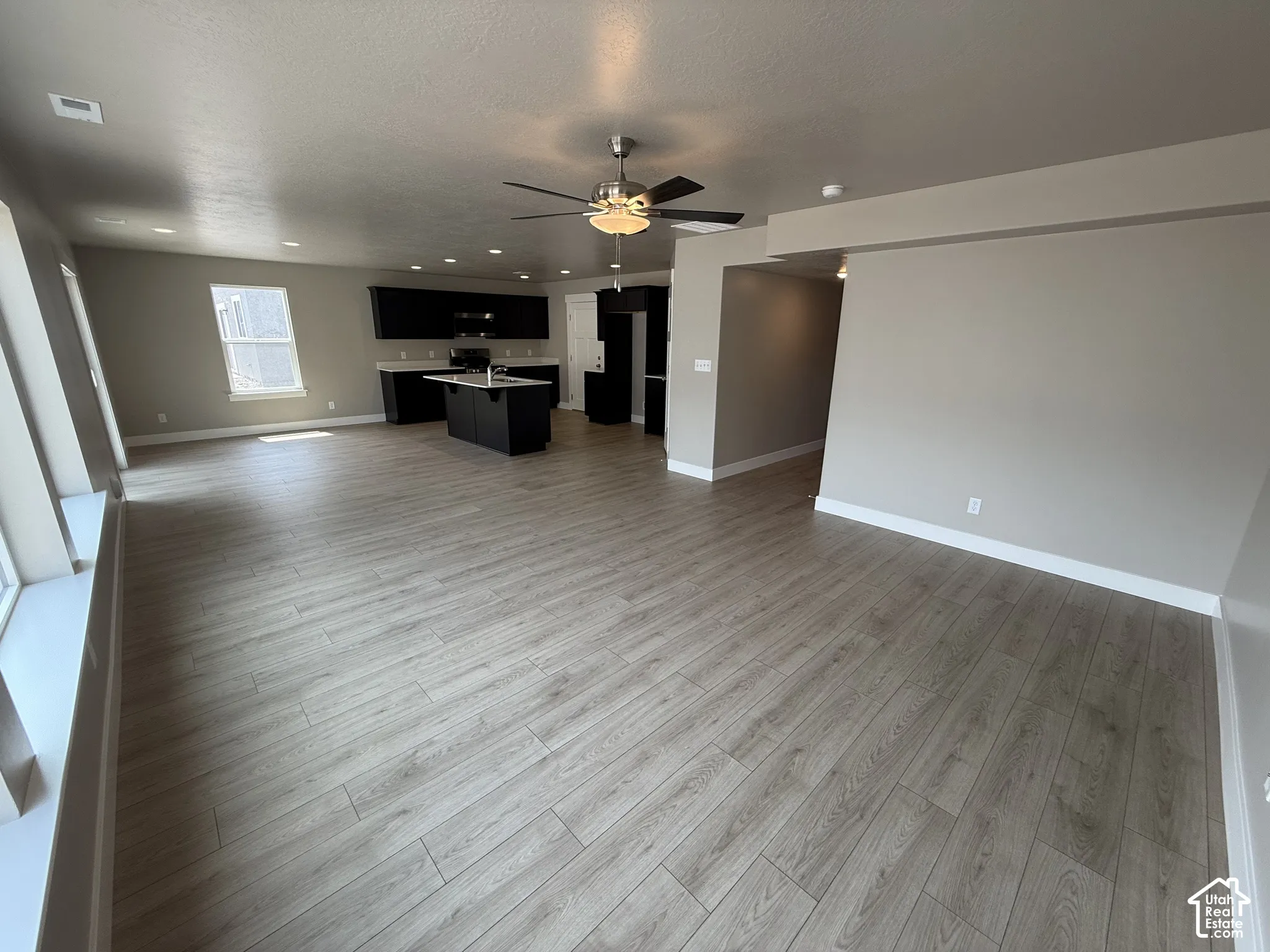 Open floor plan featuring wood-finish flooring, recessed lighting, ceiling fan, and a kitchen with dark cabinetry and a center island