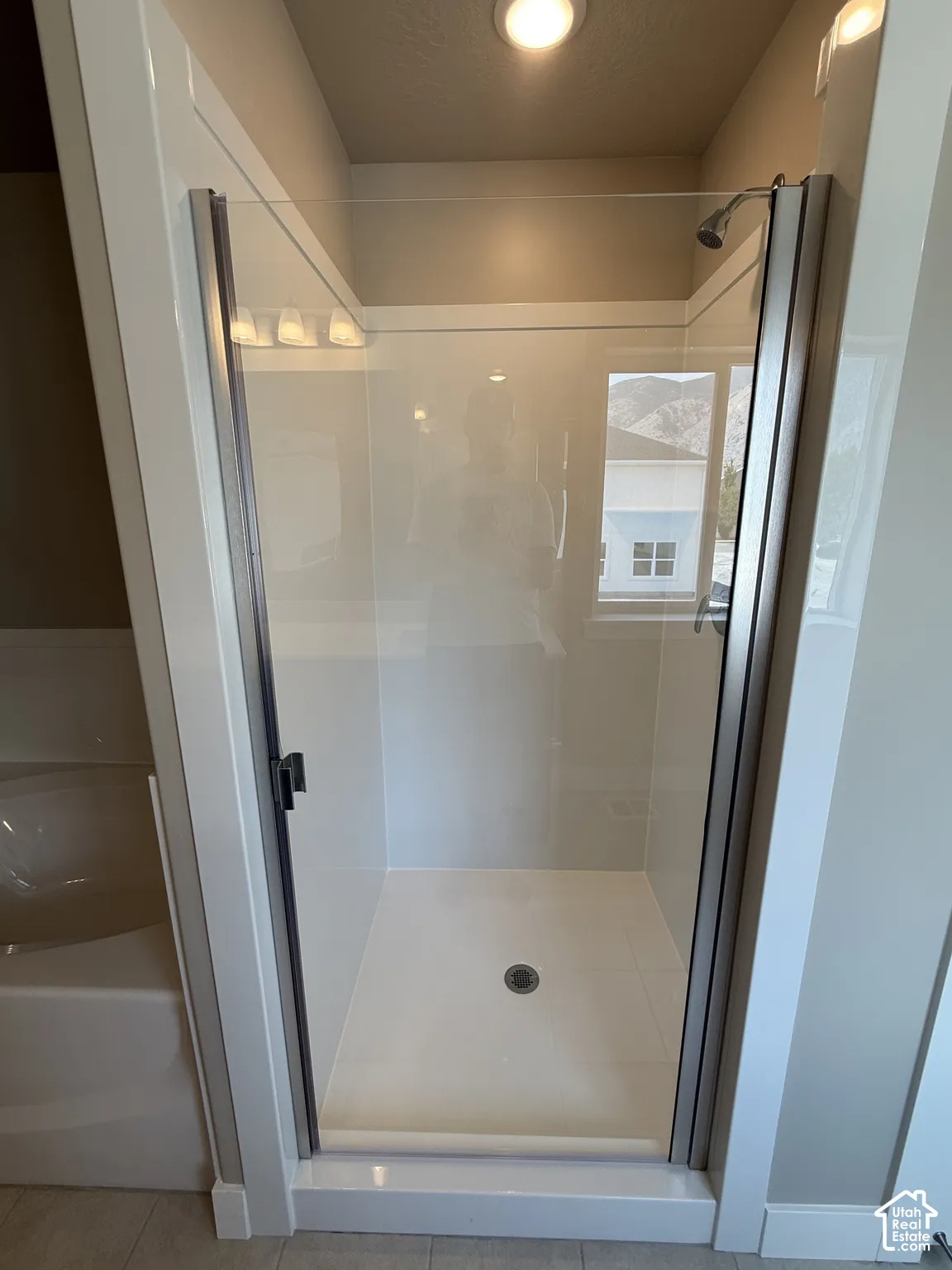 Walk-in shower enclosure featuring a glass door, metal frame, white surround, and integrated shower head