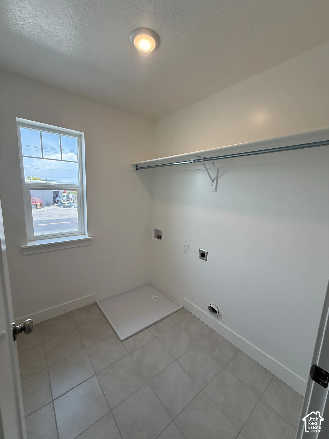 Utility room featuring tile flooring, a single-hung window, a ceiling-mounted light fixture, and an integrated hanging rod with shelf