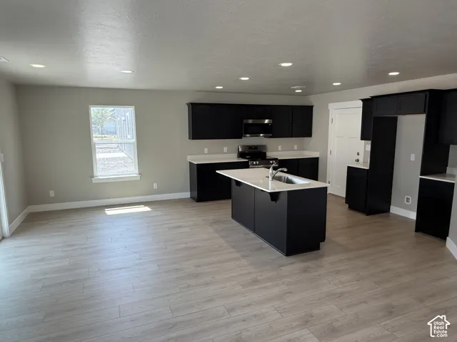 Kitchen featuring dark cabinetry, an island with a light-toned countertop, integrated stainless steel appliances, recessed lighting, and wood-finish flooring