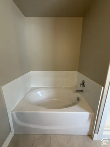 Built-in soaking tub with white surround, chrome faucet, and tile flooring