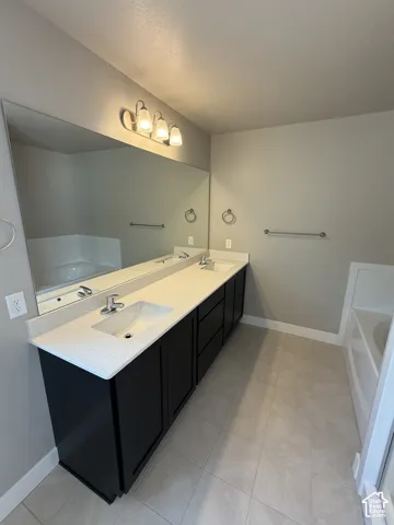 Double vanity featuring dark cabinetry, solid-surface countertop with dual rectangular sinks, a full-width mirror, and three-bulb vanity lighting