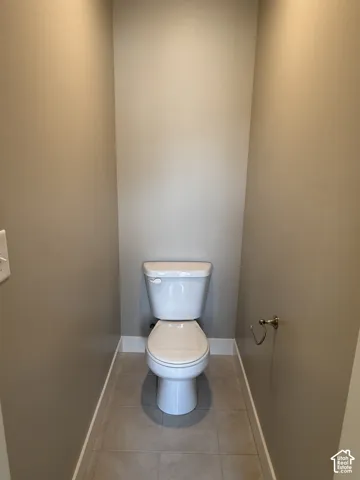 Enclosed space featuring a dual-flush toilet, neutral wall paint, and ceramic tile flooring