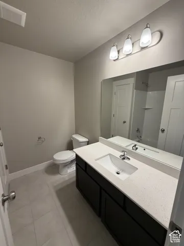 Bathroom featuring a dark-finish vanity with a light stone-composite countertop, integrated rectangular sink, large wall-mounted mirror, and tile flooring