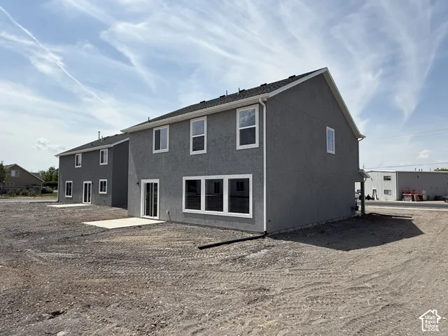 Two-story exterior featuring gray stucco siding, white trim, asphalt shingle roofing, and a concrete patio