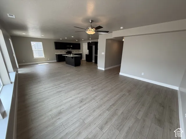 Open floor plan featuring wood-finish flooring, recessed lighting, ceiling fan, and a kitchen with dark cabinetry and a center island