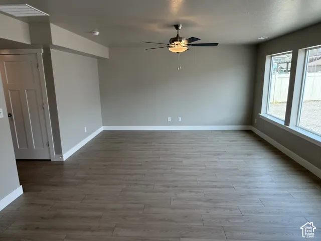 Neutral-toned interior featuring wood-finish flooring, a multi-blade ceiling fan with integrated lighting, dual windows, and a paneled interior door