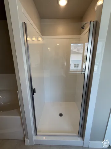 Walk-in shower enclosure featuring a glass door, metal frame, white surround, and integrated shower head