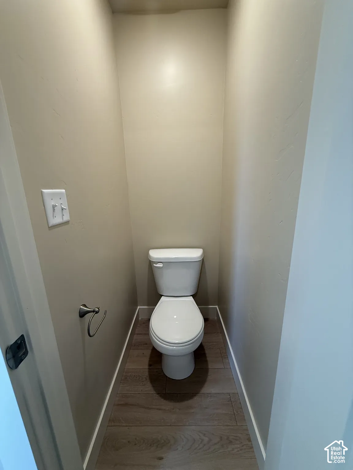 White porcelain toilet featuring a polished chrome toilet paper holder and wood-finish flooring