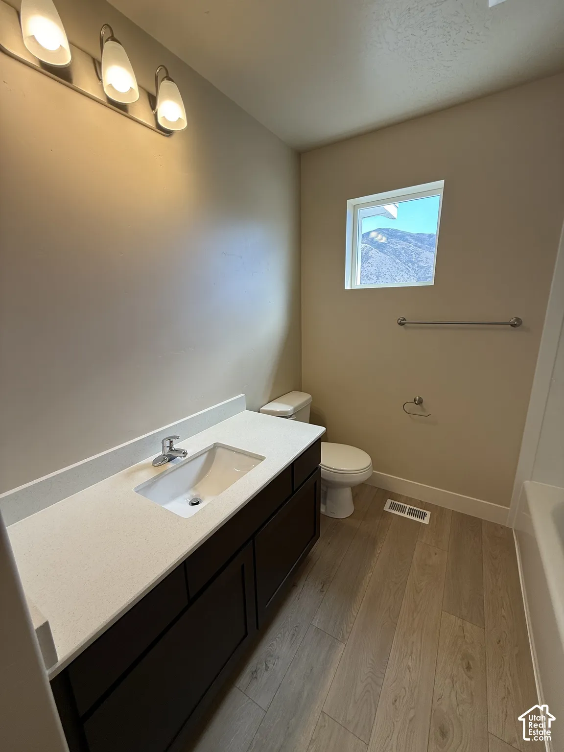 Bathroom featuring a wood-finish vanity with a stone-composite countertop, integrated rectangular basin, wood-finish flooring, and a three-light fixture