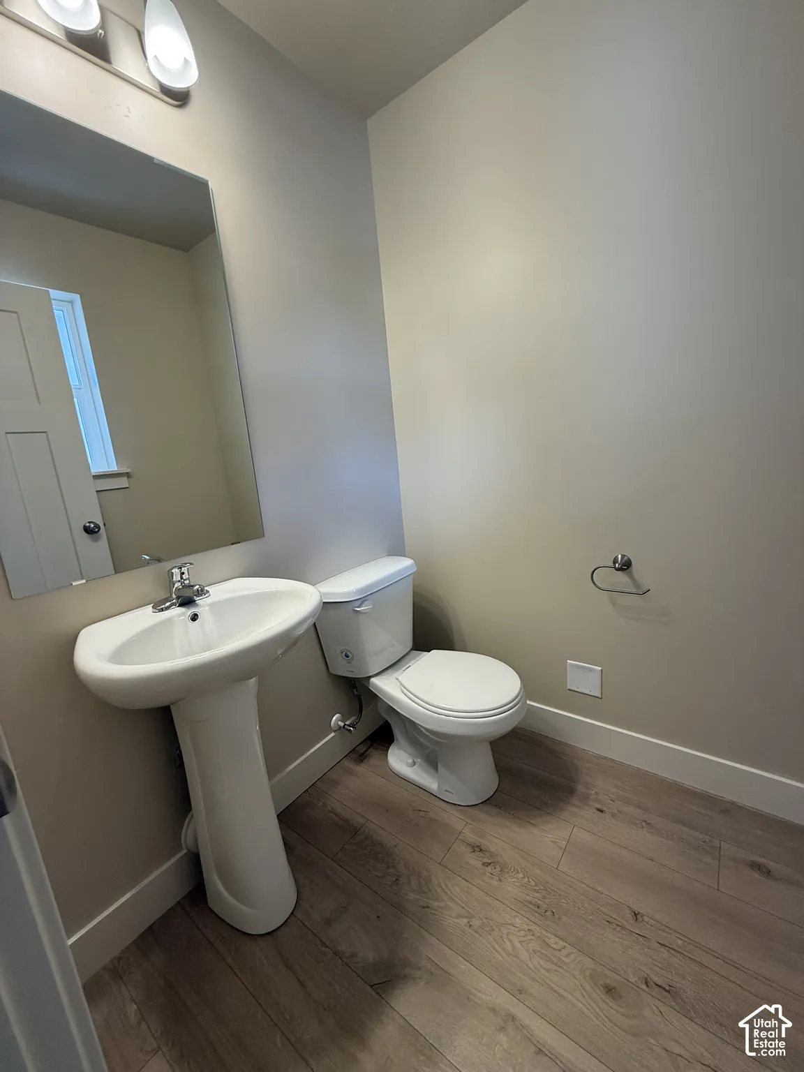 Pedestal sink with chrome faucet, large rectangular mirror, dual-light wall fixture, and wood-finish flooring