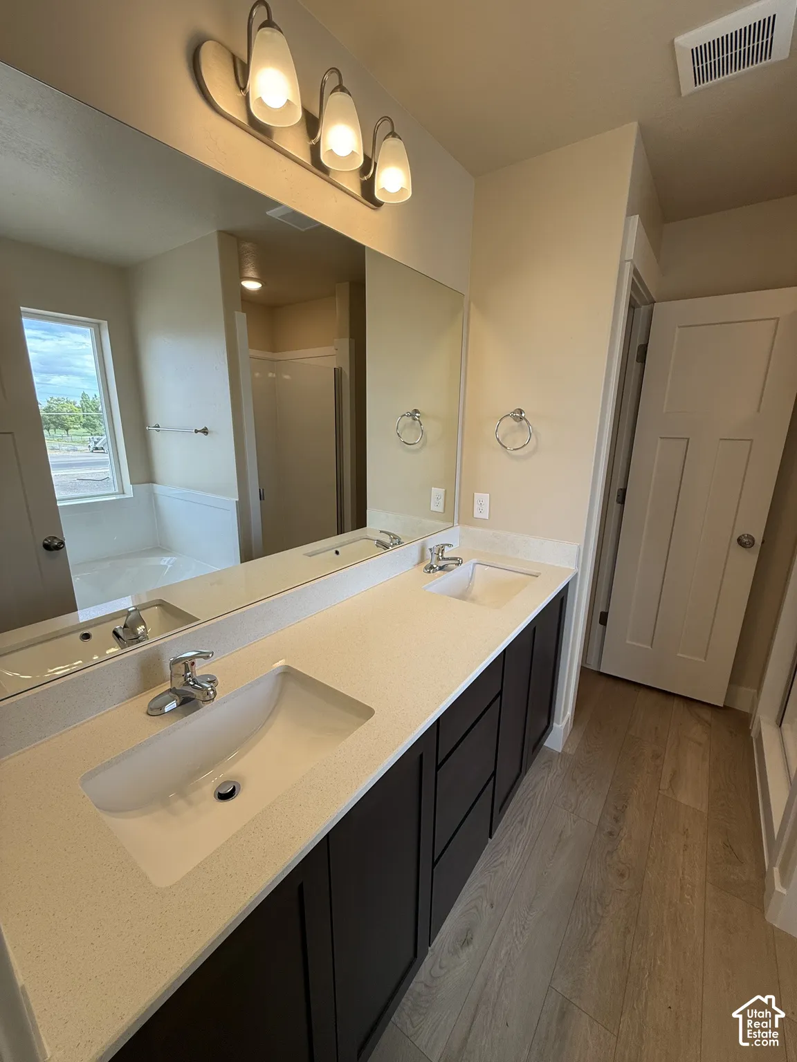 Double vanity featuring a light-toned solid surface countertop, undermount sinks, dark-finish cabinetry, and wood-finish flooring