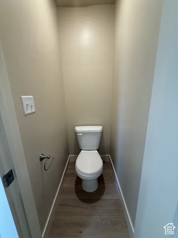 White porcelain toilet featuring a polished chrome toilet paper holder and wood-finish flooring