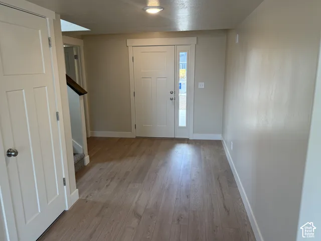 Entryway featuring light wood-finish flooring, a solid-panel door with a vertical glass sidelight, recessed ceiling lighting, and crisp white millwork trim