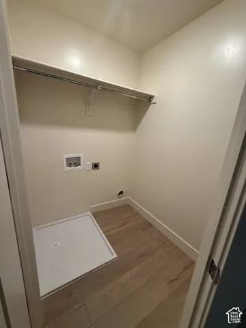 Utility space featuring wood-finish flooring, a built-in recessed laundry drain pan, and an installed overhead shelf with a integrated hanging rod
