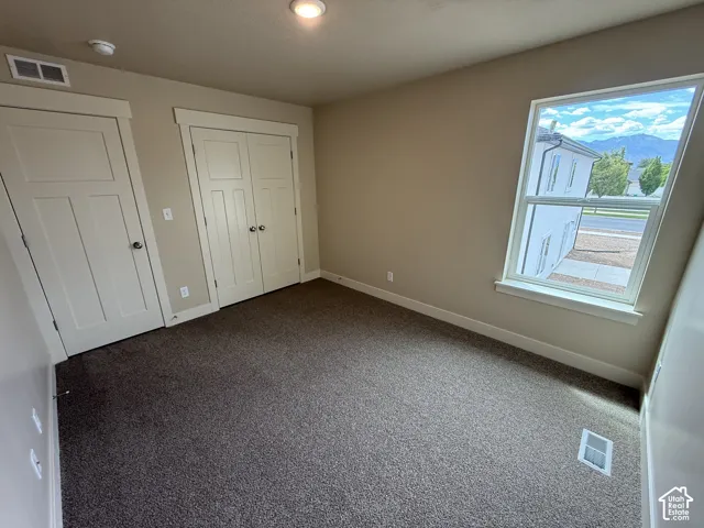 Neutral-toned walls with carpeted flooring, two paneled closet doors, and a single-hung window featuring mountain scenery