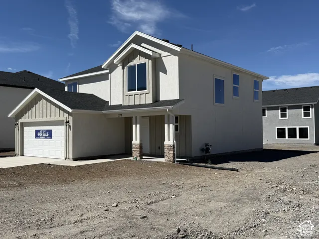 Two-story exterior featuring a mix of stucco and board-and-batten siding, stone-accented front porch columns, a concrete driveway, and an attached two-car garage