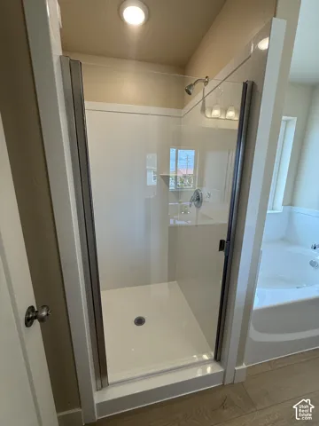 Walk-in shower with glass enclosure, chrome fixtures, built-in shelving, and white surround, accompanied by a soaking tub and wood-finish flooring