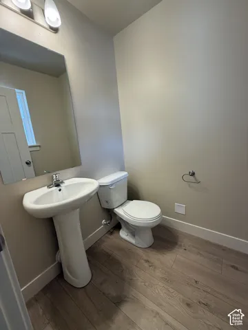 Pedestal sink with chrome faucet, large rectangular mirror, dual-light wall fixture, and wood-finish flooring