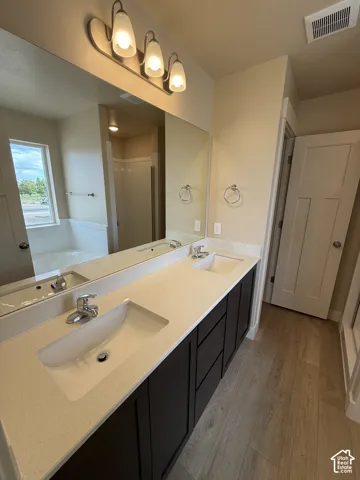 Double vanity featuring a light-toned solid surface countertop, undermount sinks, dark-finish cabinetry, and wood-finish flooring