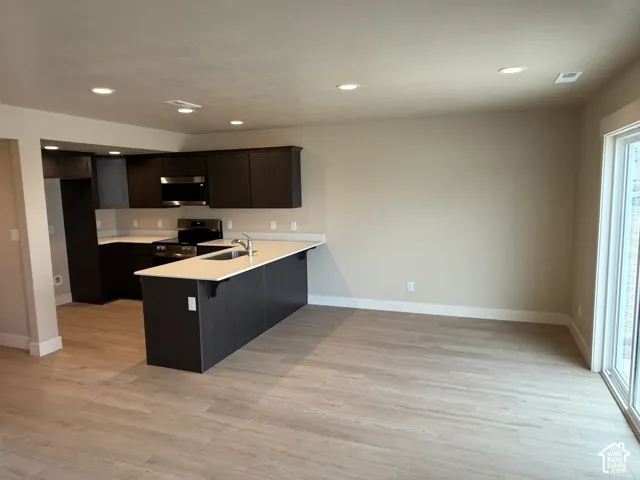 Kitchen featuring dark cabinetry, solid-surface countertops, recessed lighting, and wood-finish flooring