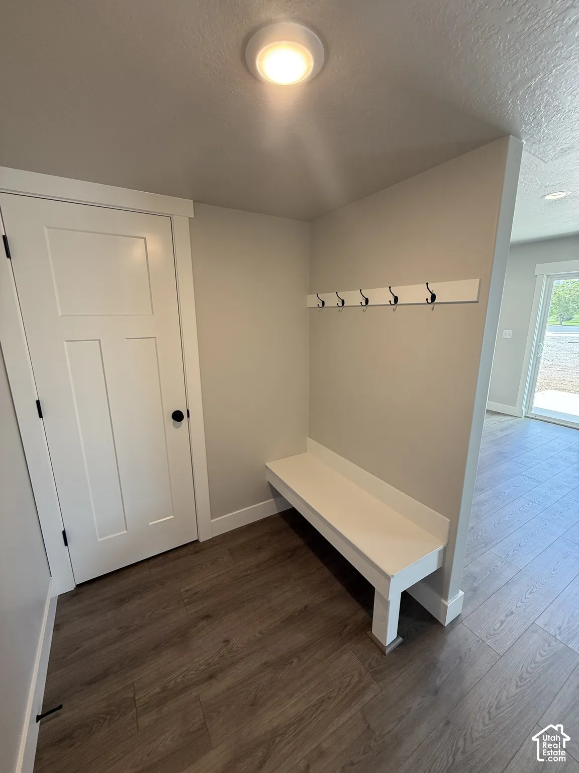 Built-in white bench, wall-mounted coat hooks, wood-finish flooring, and shaker-style door with matte black hardware