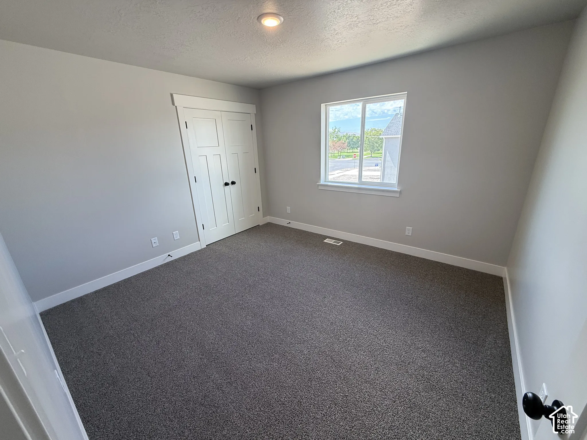 Neutral-toned interior featuring wall-to-wall carpeting, recessed ceiling lighting, a single-pane sliding window, and a closet with double-swing doors featuring matte black hardware