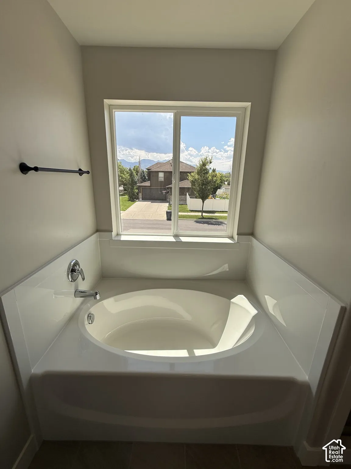 Soaking tub with a white composite surround, single-pane sliding window, chrome plumbing fixtures, and a matte black wall-mounted towel bar