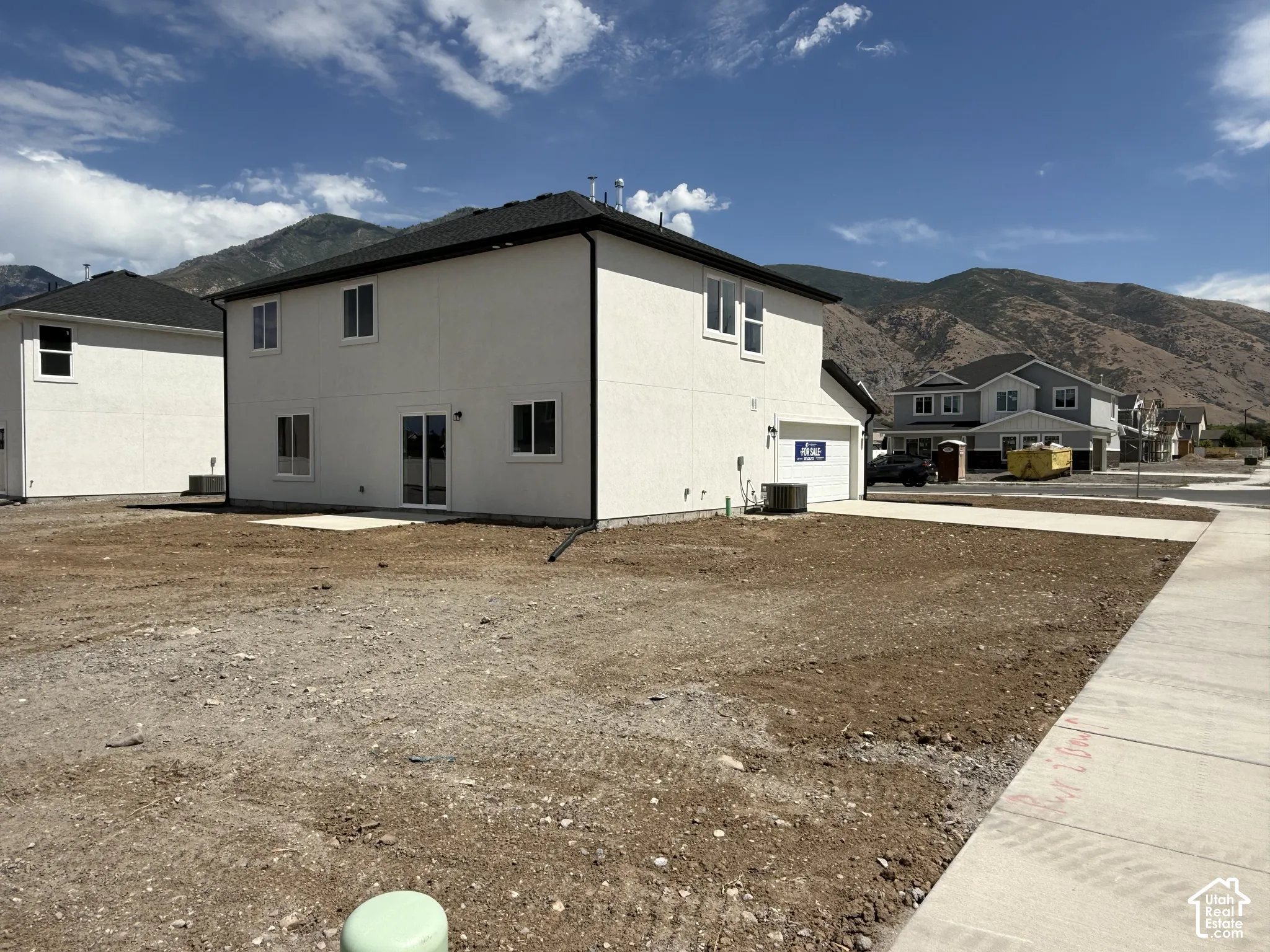 Two-story exterior featuring light-toned stucco siding, a dark-shingled roof, sliding glass doors, a concrete driveway, and an expansive mountain backdrop