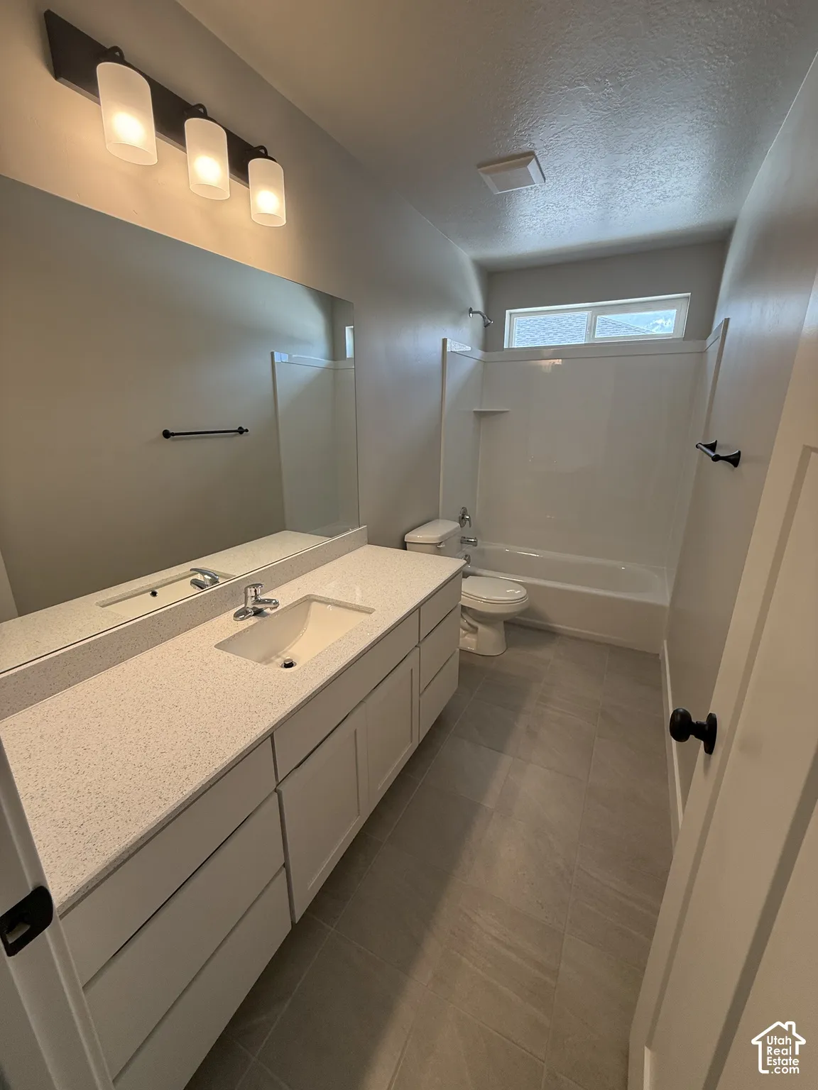 Bathroom featuring a wide vanity with a solid surface countertop, integrated sink, three-light fixture, grey tile flooring, and a shower-tub combination with a white surround