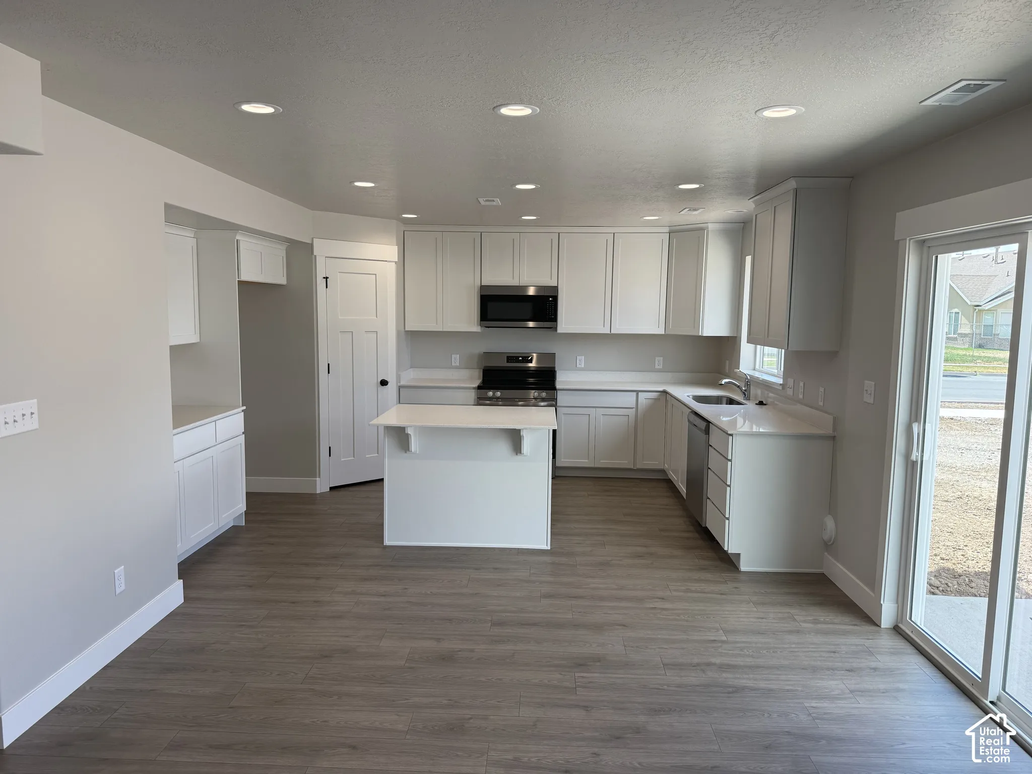 Kitchen featuring white shaker-style cabinetry, quartz countertops, a central island, recessed lighting, and wood-finish flooring