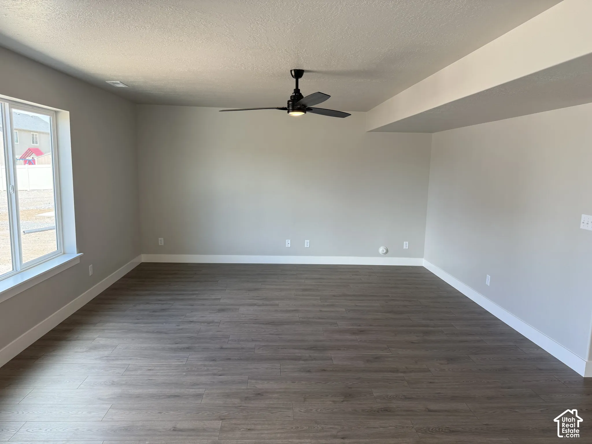 Neutral-toned interior featuring wood-finish flooring, a matte black ceiling fan, recessed lighting, and a large window with a white frame