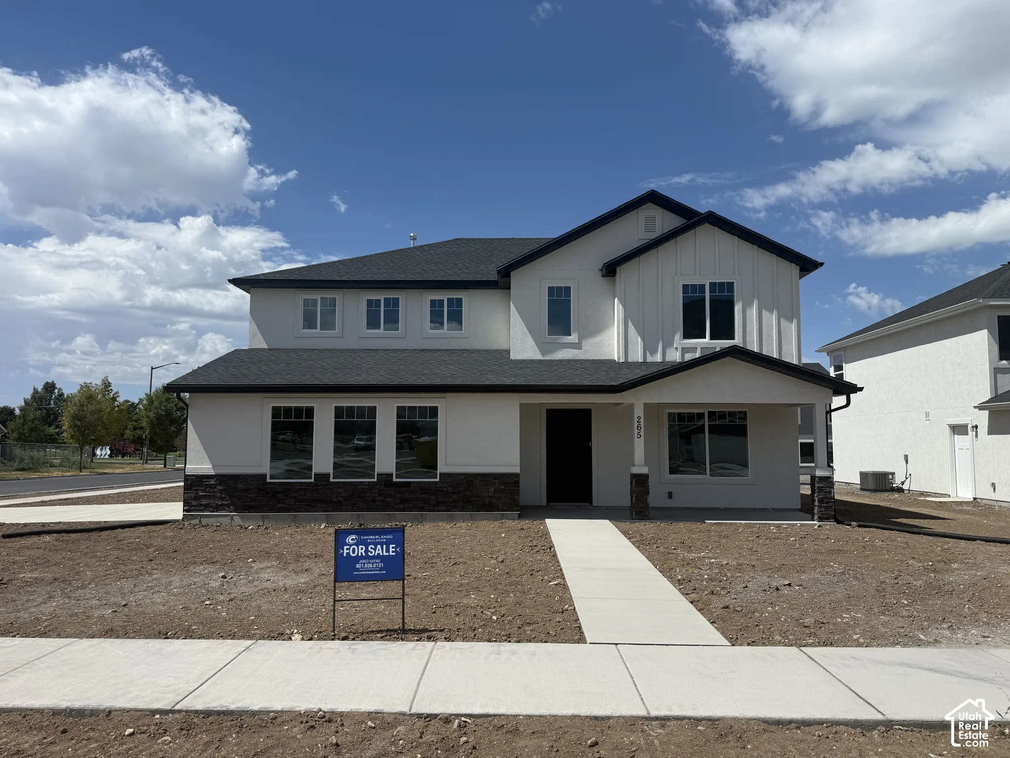 Two-story exterior featuring a mix of white vertical board-and-batten siding and stone masonry, a covered entryway, and a dark shingle roof