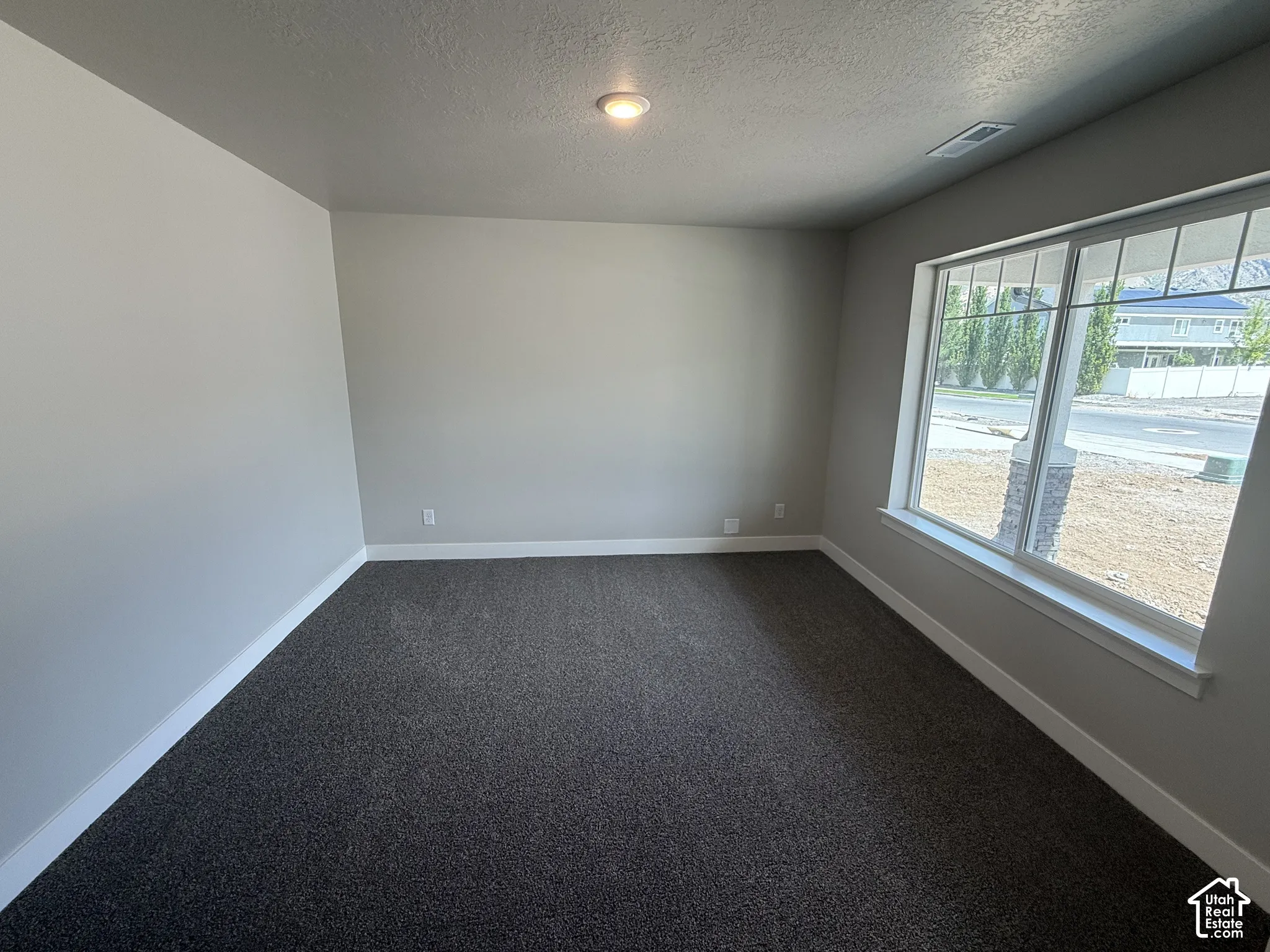 Neutral-toned interior space featuring dark wall-to-wall carpeting, expansive windows with grid detailing, and recessed ceiling lighting