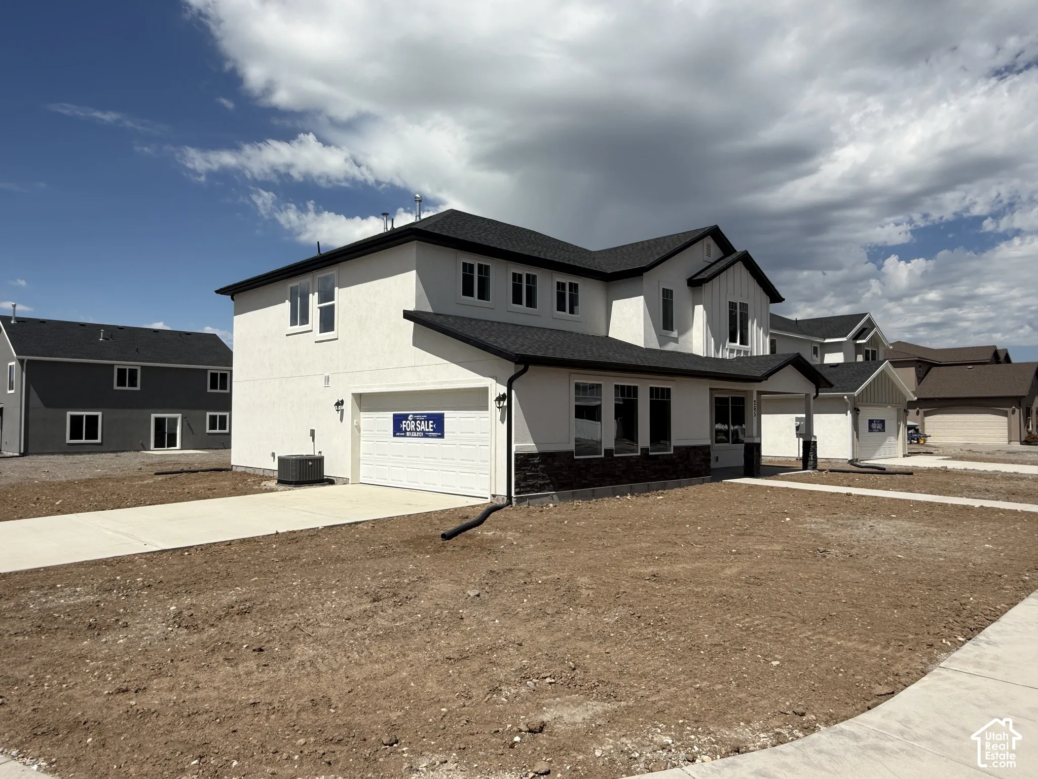 Two-story residence featuring a multi-textured exterior of smooth stucco and dark stone veneer, an attached garage, and a concrete driveway