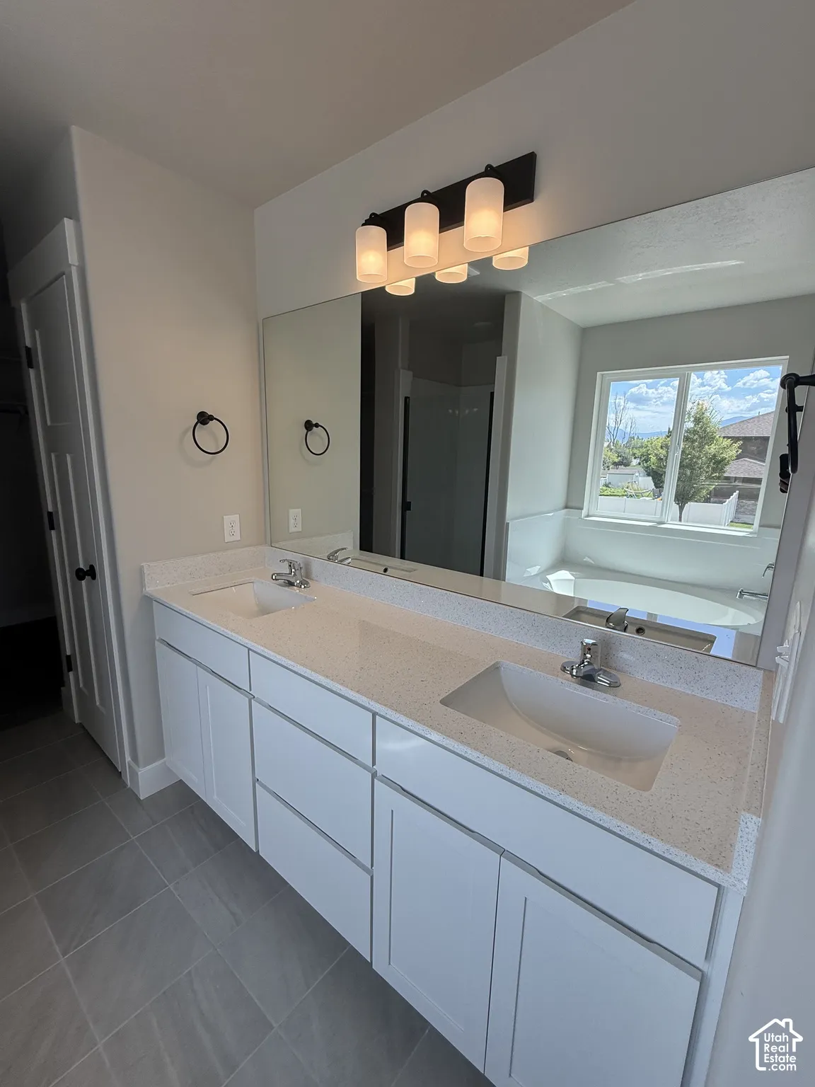 Double vanity featuring white cabinetry, quartz-finish countertops, undermount sinks, expansive wall-mounted mirror, and multi-light vanity fixture