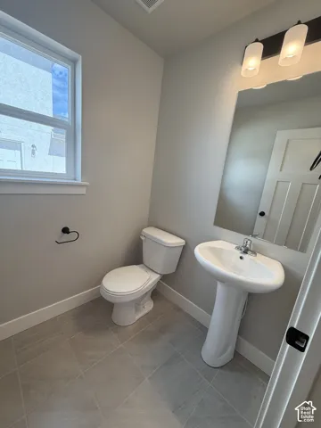 Powder room featuring a pedestal sink, ceramic tile flooring, a large wall-mounted mirror, and a three-light vanity fixture