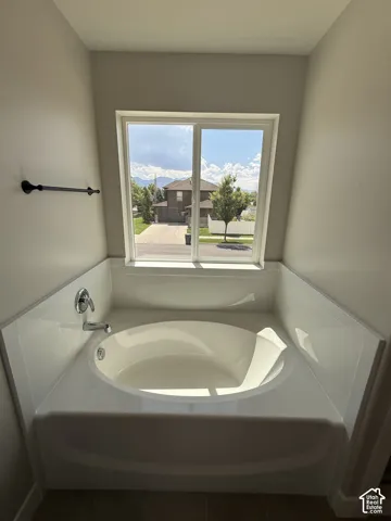 Soaking tub with a white composite surround, single-pane sliding window, chrome plumbing fixtures, and a matte black wall-mounted towel bar
