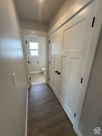 Hallway featuring wood-finish flooring, white shaker-style doors with matte black hardware, and crisp white millwork trim