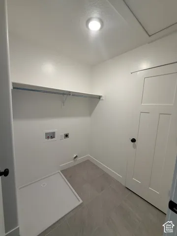 Utility space featuring ceramic tile flooring, a recessed floor drain, built-in shelving with a clothes rod, and a multi-panel door with matte black hardware
