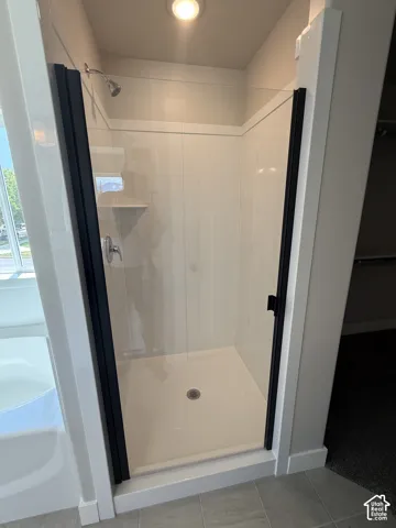 Walk-in shower featuring a glass enclosure with matte black framing, white panel surround, built-in shelving, and a chrome shower head