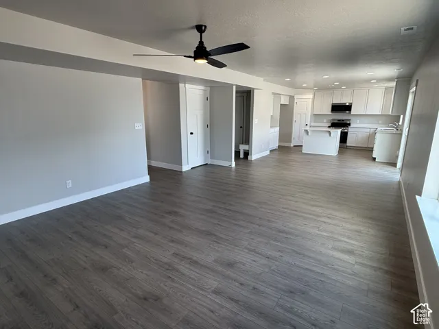 Open-concept interior featuring wood-finish flooring, recessed lighting, a matte black ceiling fan, white cabinetry with an integrated kitchen island, and shaker-style interior doors