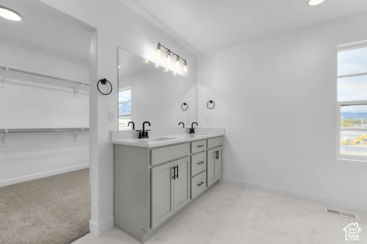 Dual-sink vanity featuring a light gray finish, solid-surface countertop, and matte black hardware, paired with a full-width mirror and integrated five-light fixture